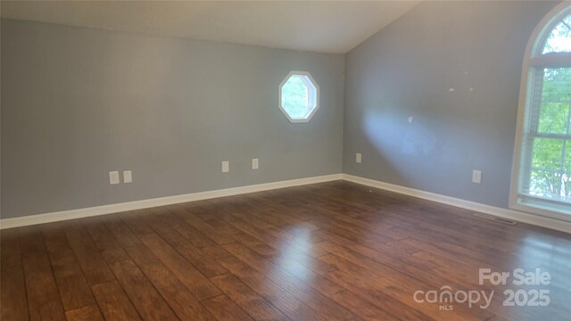 spare room with dark wood-style floors, baseboards, and vaulted ceiling
