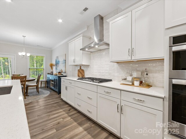 603 Southstone Dr, Matthews, NC 28104 - kitchen with wall chimney exhaust hood, stainless steel gas stovetop, crown molding, light wood-type flooring, and a chandelier