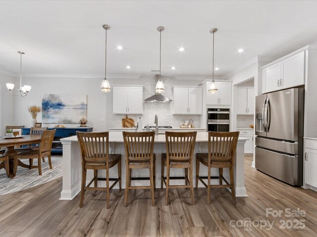 603 Southstone Dr, Matthews, NC 28104 - kitchen featuring stainless steel appliances, wall chimney exhaust hood, light countertops, tasteful backsplash, and a kitchen island with sink