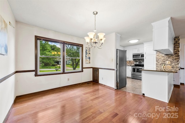 113 Helena St, Mount Holly, NC 28120 - kitchen with appliances with stainless steel finishes, dark countertops, light wood finished floors, tasteful backsplash, and a chandelier