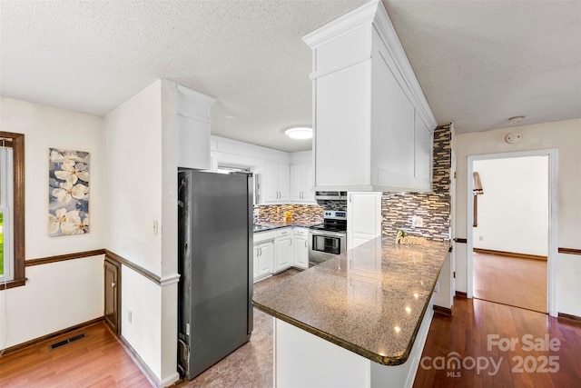 113 Helena St, Mount Holly, NC 28120 - kitchen featuring appliances with stainless steel finishes, a peninsula, backsplash, white cabinets, and wood finished floors