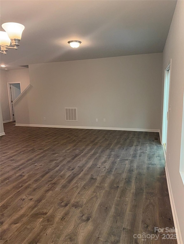 empty room with dark wood-type flooring, baseboards, and a chandelier