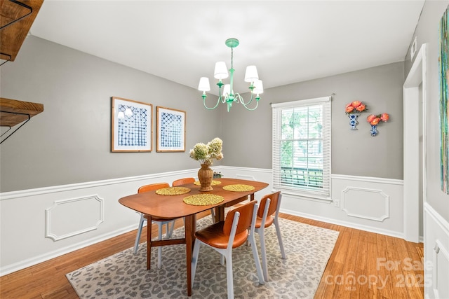 dining room featuring wainscoting, a chandelier, light wood finished floors, and a decorative wall