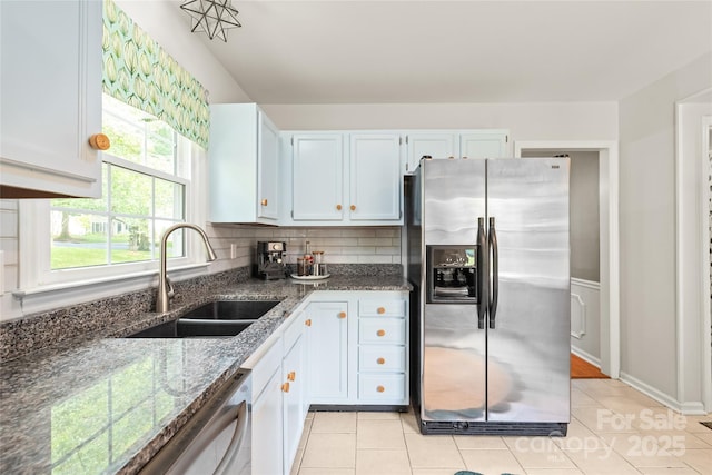 kitchen with appliances with stainless steel finishes, a sink, dark stone countertops, light tile patterned flooring, and backsplash