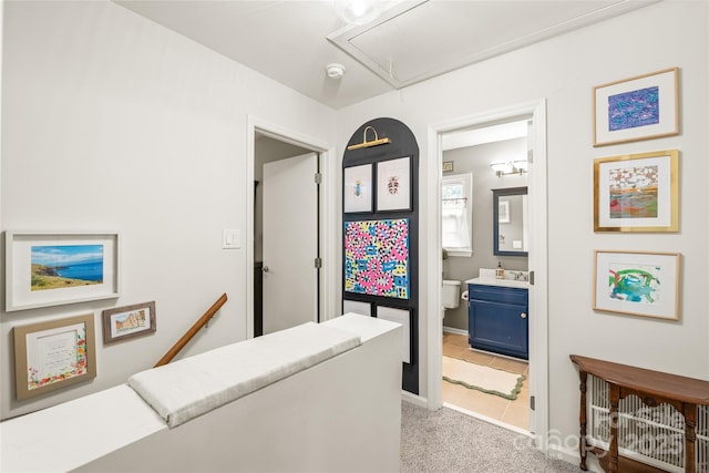 hallway featuring attic access, light colored carpet, an upstairs landing, and baseboards