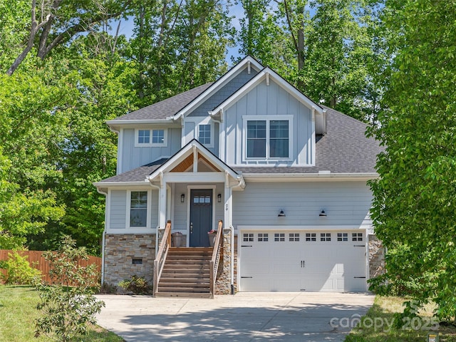 craftsman-style home featuring board and batten siding, driveway, fence, stone siding, and a garage