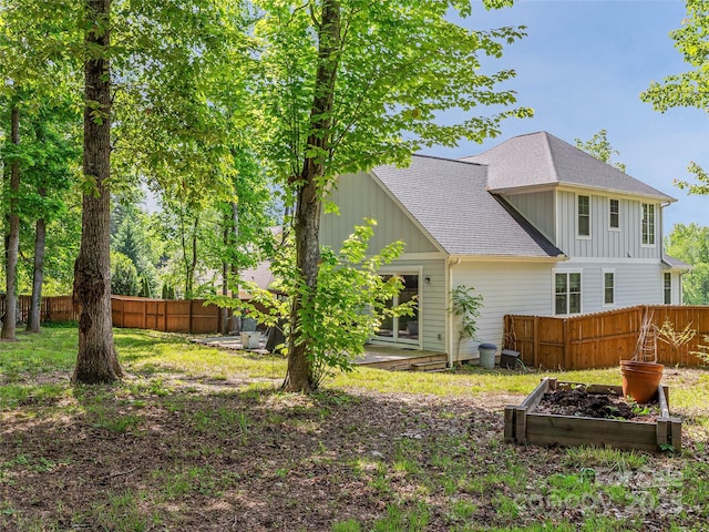 back of property with a shingled roof, board and batten siding, a fenced backyard, and a garden
