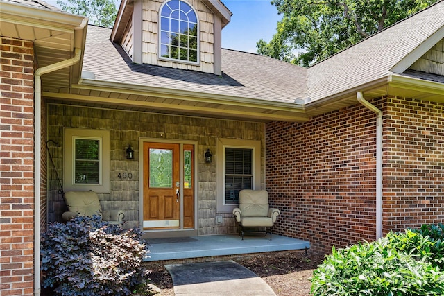 doorway to property with a shingled roof, covered porch, and brick siding