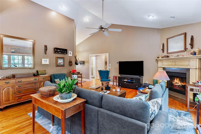 living area featuring a ceiling fan, light wood-style flooring, a lit fireplace, high vaulted ceiling, and recessed lighting