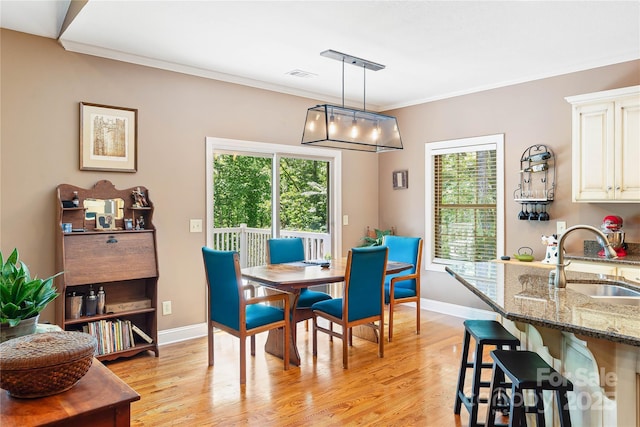 dining room with crown molding, healthy amount of natural light, light wood finished floors, and baseboards