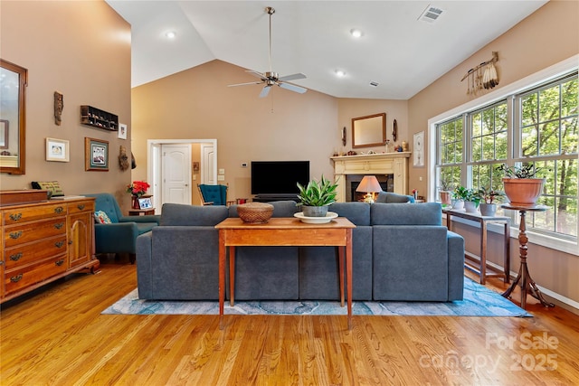 living room with a ceiling fan, light wood-type flooring, high vaulted ceiling, a warm lit fireplace, and recessed lighting
