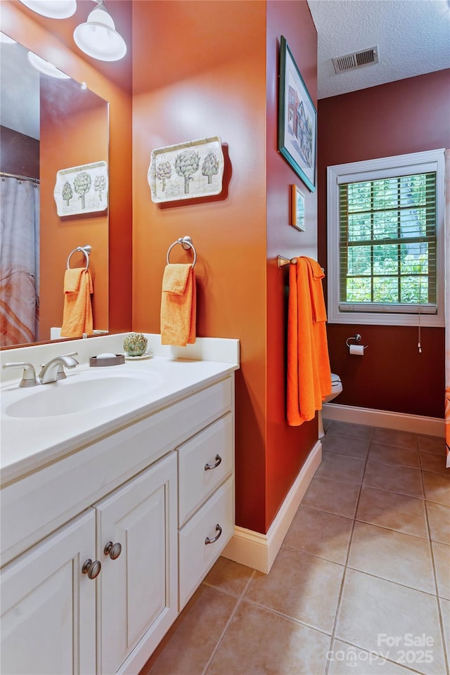 full bathroom with tile patterned flooring, vanity, toilet, baseboards, and a textured ceiling