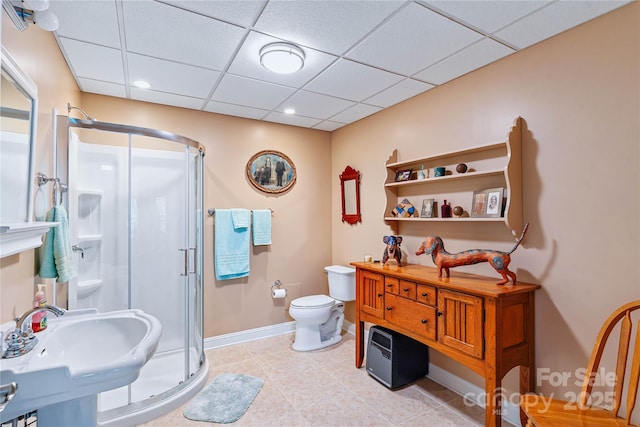 bathroom featuring a stall shower, a drop ceiling, toilet, baseboards, and a sink