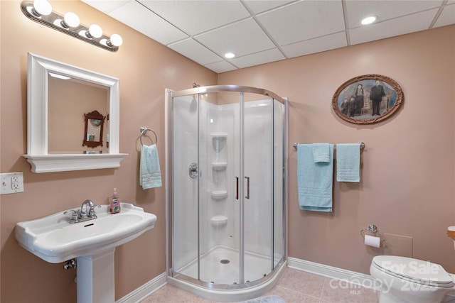 bathroom featuring baseboards, a stall shower, tile patterned flooring, toilet, and a paneled ceiling