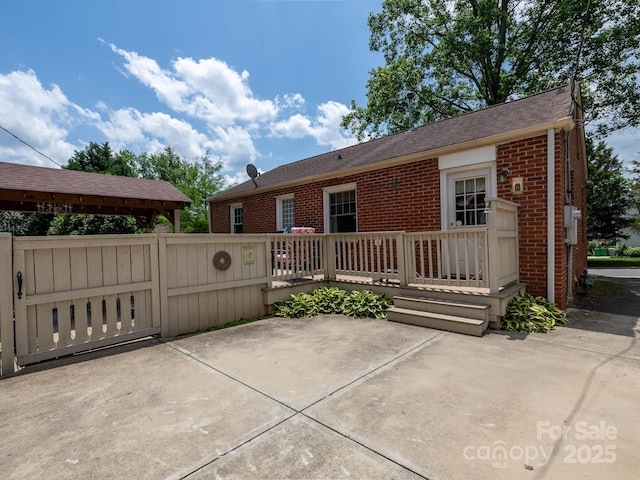 view of front of home featuring brick siding, a patio, roof with shingles, and a wooden deck