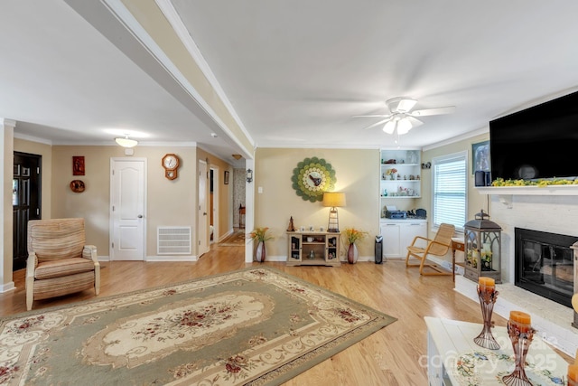 living area with wood finished floors, a fireplace, a ceiling fan, ornamental molding, and baseboards