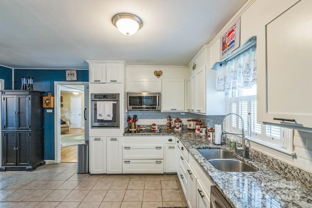 kitchen with appliances with stainless steel finishes, a sink, decorative backsplash, light tile patterned floors, and white cabinets