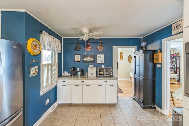 kitchen featuring freestanding refrigerator, ceiling fan, white cabinets, light tile patterned flooring, and light stone countertops