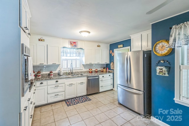 kitchen with appliances with stainless steel finishes, a sink, backsplash, white cabinetry, and light tile patterned flooring
