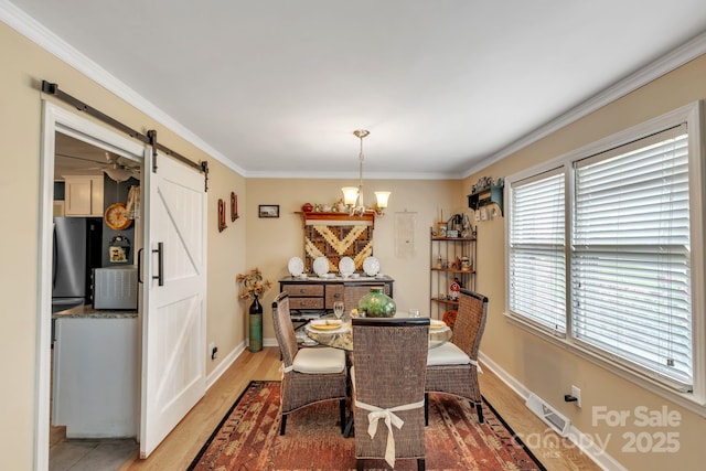dining room with a barn door, a chandelier, crown molding, baseboards, and light wood-style floors