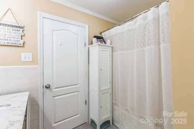 bathroom with tile walls, ornamental molding, vanity, a wainscoted wall, and curtained shower