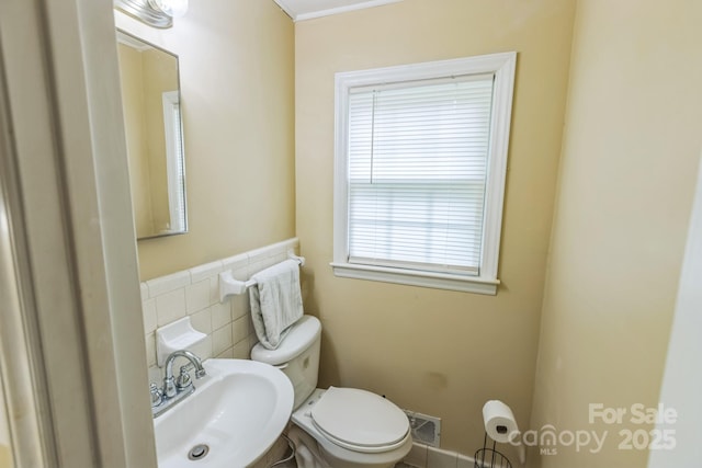 bathroom featuring a sink, toilet, tile walls, and a wainscoted wall