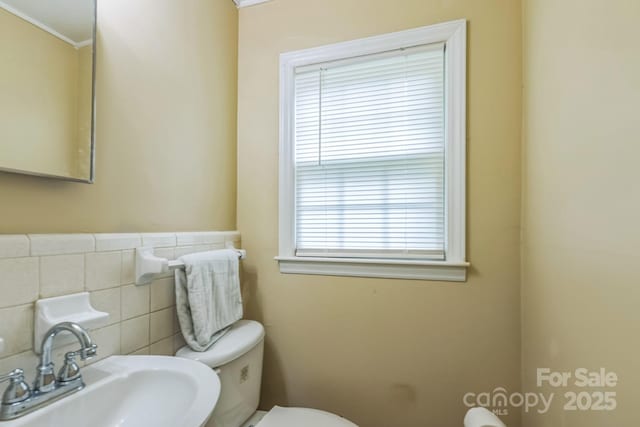 half bathroom featuring a sink, toilet, tile walls, and crown molding