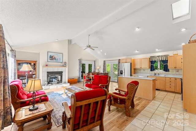 living area with a tiled fireplace, light wood-style floors, ceiling fan, and a textured ceiling