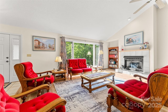 living area featuring a tiled fireplace, ceiling fan, and high vaulted ceiling