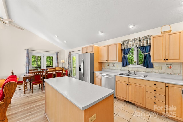 kitchen with appliances with stainless steel finishes, a sink, light brown cabinetry, vaulted ceiling, and a kitchen island