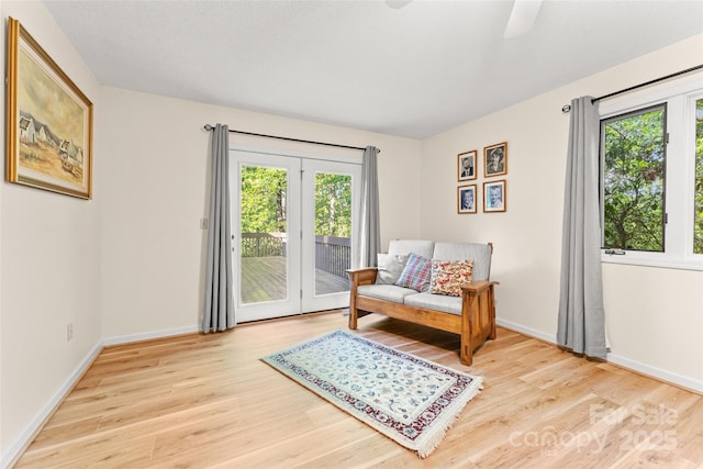 living area featuring healthy amount of natural light, wood finished floors, a ceiling fan, and baseboards