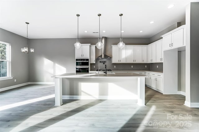 7517 Lancaster Hwy Unit 5, Waxhaw, NC 28173 - kitchen featuring wall chimney range hood, light wood-style flooring, decorative backsplash, stainless steel double oven, and a kitchen island with sink