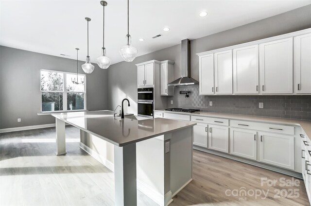 7517 Lancaster Hwy Unit 5, Waxhaw, NC 28173 - kitchen with wall chimney exhaust hood, stainless steel gas stovetop, light wood-type flooring, decorative backsplash, and an island with sink