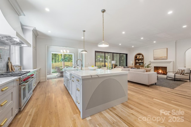 kitchen featuring a sink, double oven range, premium range hood, gray cabinets, and light wood-style flooring