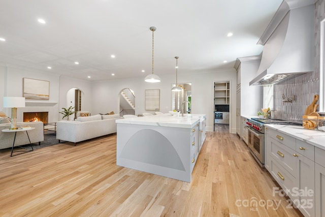 kitchen with range with two ovens, custom range hood, crown molding, a lit fireplace, and light wood finished floors