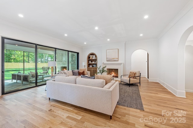 living room with arched walkways, ornamental molding, a warm lit fireplace, recessed lighting, and light wood-style flooring