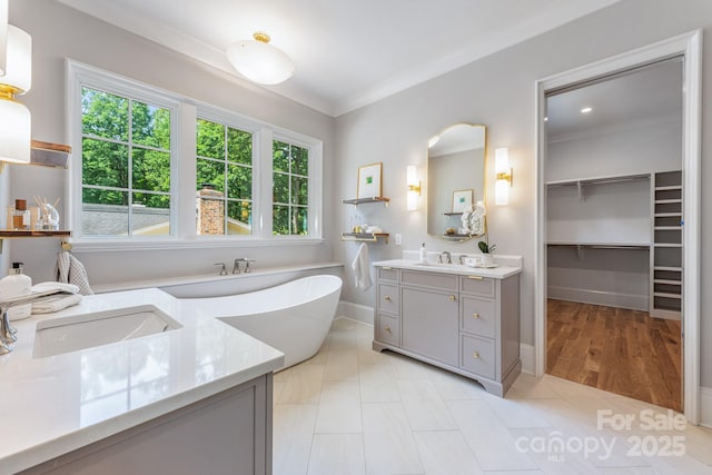 bathroom with two vanities, ornamental molding, a soaking tub, and baseboards