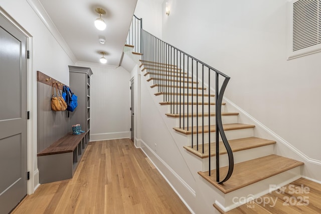 stairs featuring wood finished floors, ornamental molding, and baseboards