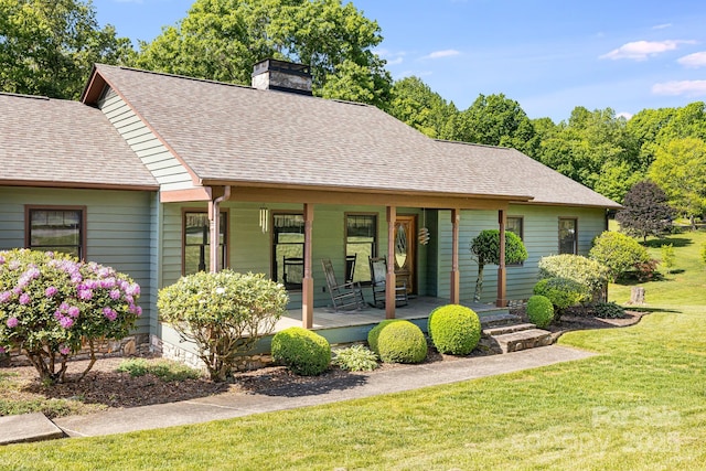 view of front facade featuring covered porch, a chimney, a front yard, and a shingled roof
