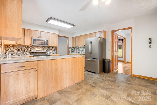 kitchen featuring stainless steel appliances, a sink, light brown cabinets, a peninsula, and decorative backsplash