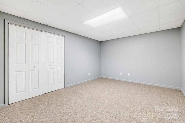 unfurnished bedroom featuring carpet flooring, a closet, baseboards, and a paneled ceiling