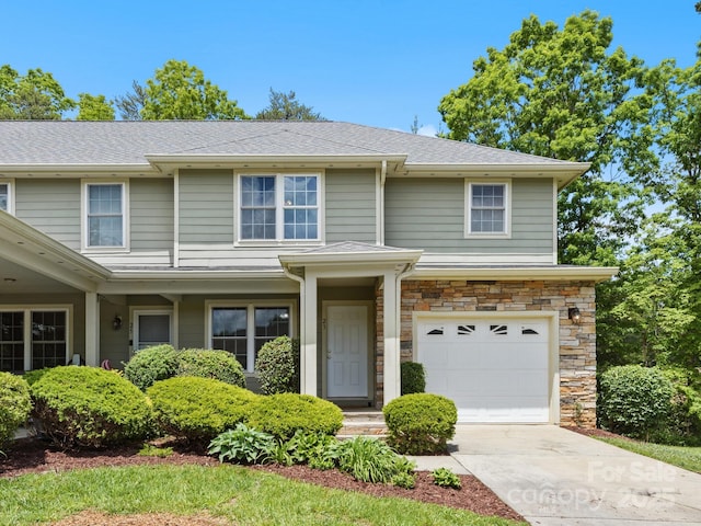 view of front of home with an attached garage, stone siding, concrete driveway, and roof with shingles