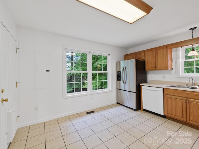 kitchen with white dishwasher, a sink, stainless steel fridge, light countertops, and brown cabinets