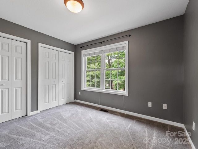 unfurnished bedroom featuring multiple closets, baseboards, and carpet