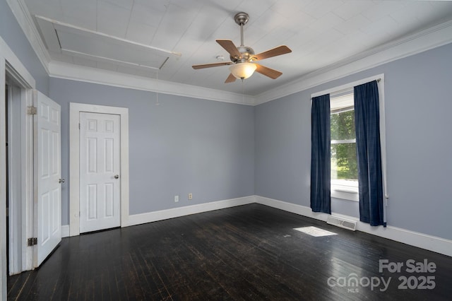 empty room featuring attic access, a ceiling fan, dark wood-type flooring, baseboards, and crown molding