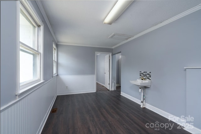 empty room featuring attic access, wood finished floors, a wainscoted wall, and crown molding