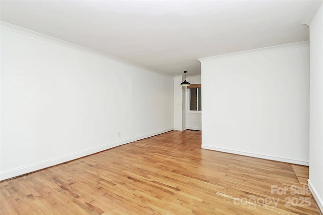 empty room featuring ornamental molding, light wood finished floors, and baseboards