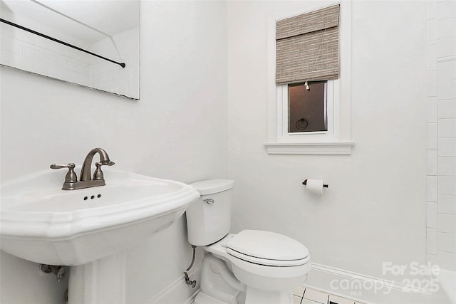 bathroom featuring baseboards, toilet, a sink, and tile patterned flooring