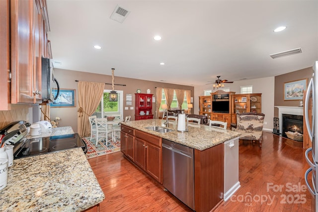 kitchen with stainless steel appliances, a sink, an island with sink, open floor plan, and a ceiling fan
