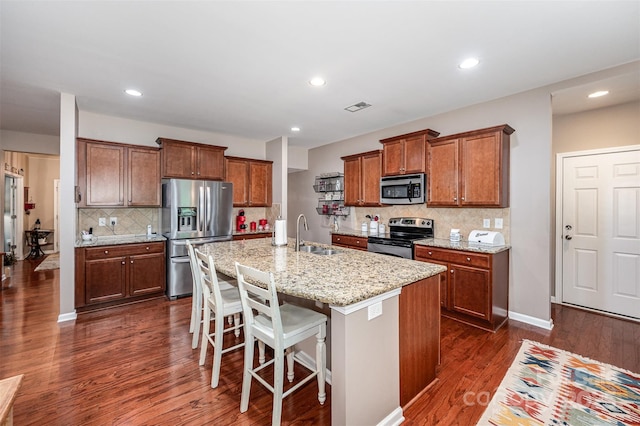 kitchen with stainless steel appliances, a sink, brown cabinetry, dark wood-style flooring, and backsplash
